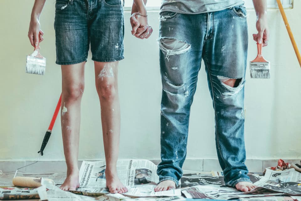 Two painters in paint-splattered jeans holding brushes