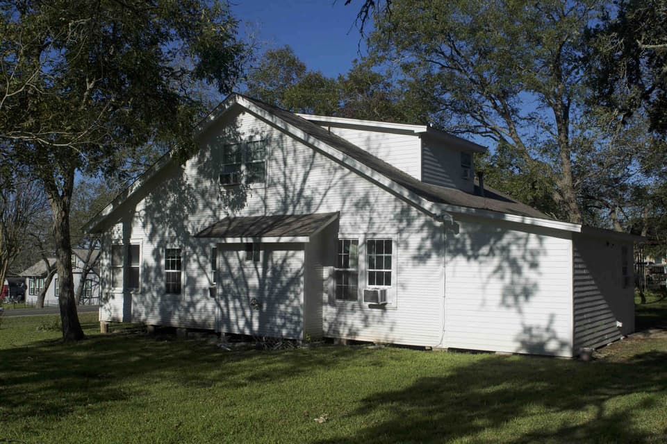 Side view of a white renovated house with dark window trim on a sunny lawn